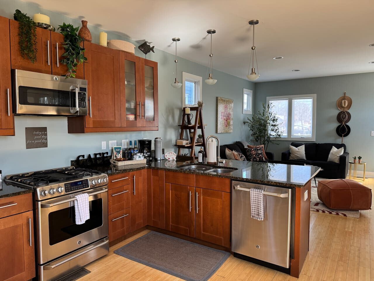 A modern kitchen with a central island, stainless steel appliances, wooden cabinets, and a dining area with a black sofa and side tables.