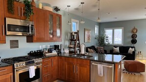 Une cuisine moderne dotée d’un îlot central, d’appareils électroménagers en acier inoxydable, de meubles de rangement en bois et d’un coin repas avec un canapé noir et des tables d’appoint.