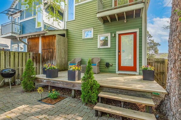A two-story house with a green exterior, a wooden deck, and a red door.
