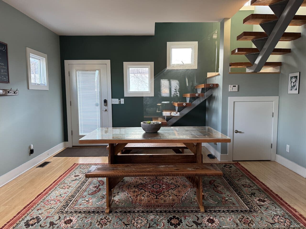 A dining area with a wooden table and bench, a patterned rug, and a staircase with wooden beams.