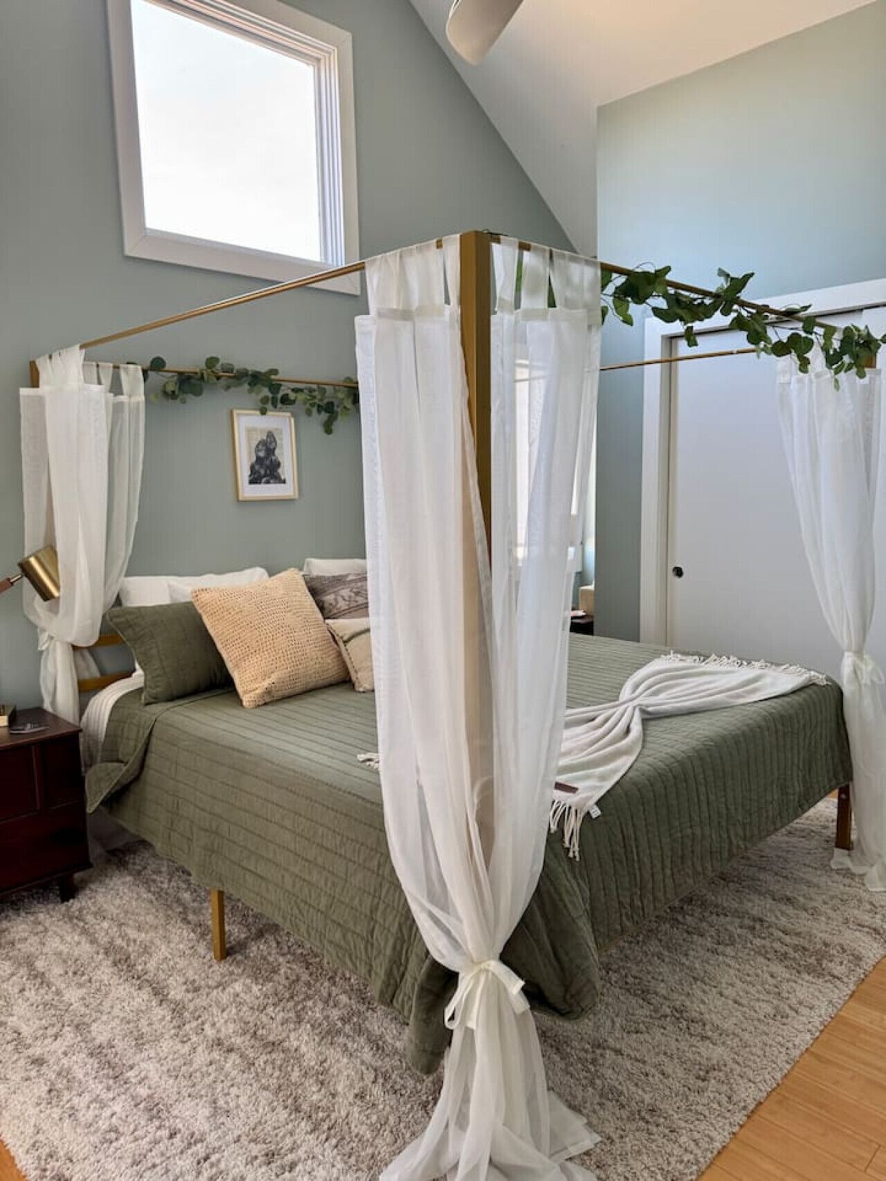 A bedroom with a green bedspread, white canopy bed, and a small bedside table.