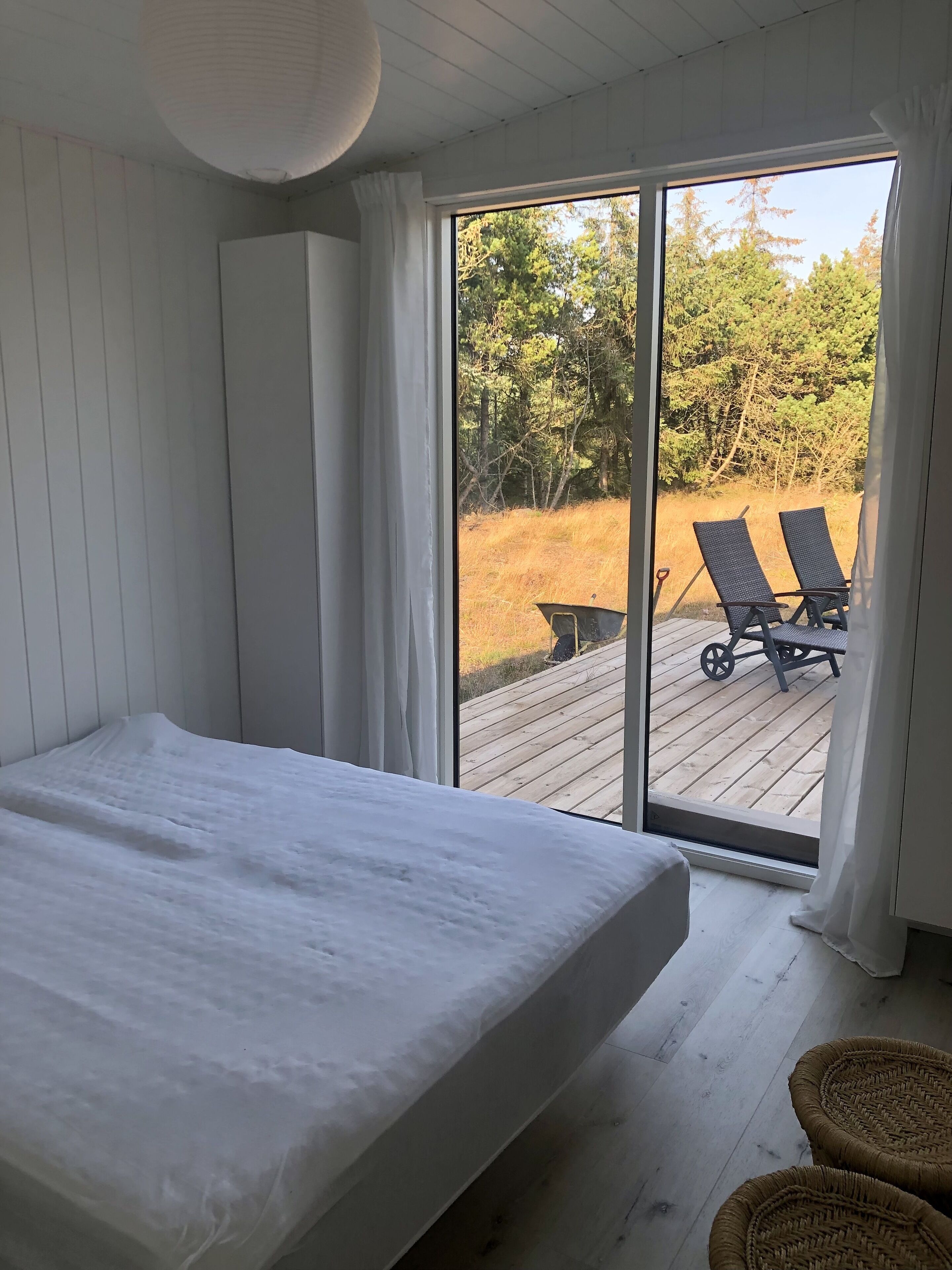 A bedroom with a large bed, a sliding glass door leading to an outdoor deck with two lounge chairs and a table.