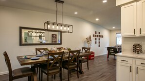 A dining area with a wooden table, chairs, and a chandelier. There is a kitchen area with white cabinets and a countertop. - Uptown Area! Putting Green-BBQ-Hot Tub-Game Room (Albuquerque)