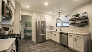 A modern kitchen with white cabinets, stainless steel appliances, and a wooden floor. - Uptown Area! Putting Green-BBQ-Hot Tub-Game Room (Albuquerque)