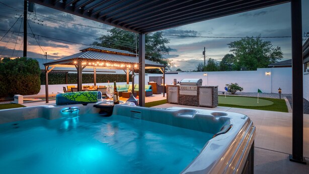 A hot tub with a pergola and outdoor seating area, a barbecue grill, and a well-maintained lawn. - Uptown Area! Putting Green-BBQ-Hot Tub-Game Room (Albuquerque)