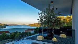 Ein Balkon mit Tisch und Stühlen, mit Blick auf ein Gewässer und Hügel.