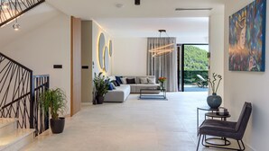 Ein modernes Wohnzimmer mit Sofa, Couchtisch und Sessel. Eine Treppe mit Geländer und ein Blumentopf sind ebenfalls zu sehen.