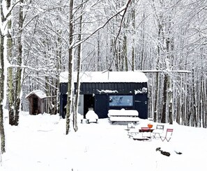 A cabin in a snowy forest with a small shed and a bench.