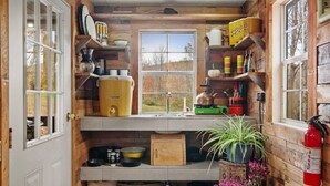A kitchen with wooden walls, a window, and various kitchen items. - Off-Grid Tiny Cabin with Cozy Vintage Charm (Bovina)