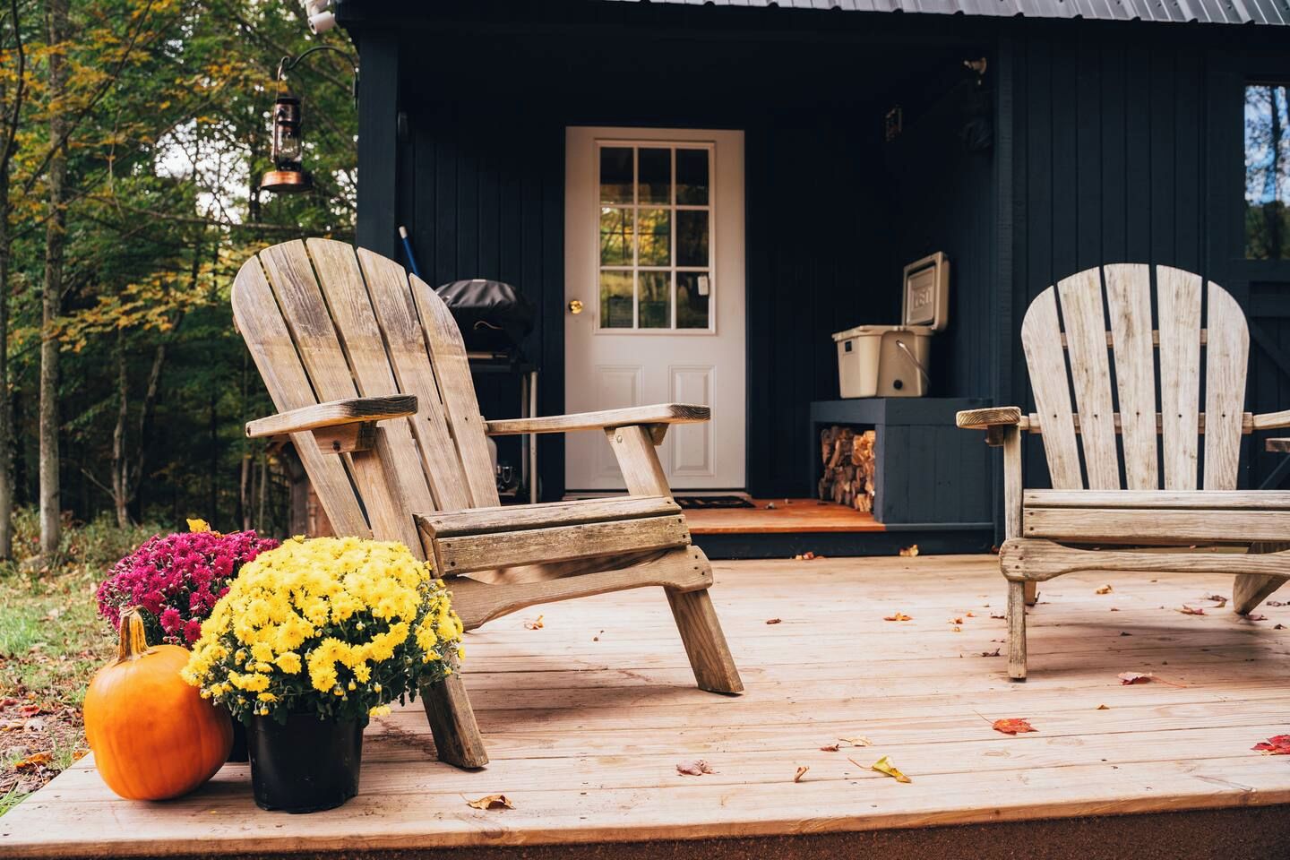 Una terraza de madera con dos sillas Adirondack, una calabaza y una planta en maceta con flores amarillas.