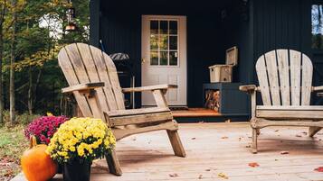 Una terraza de madera con dos sillas Adirondack, una calabaza y una planta en maceta con flores amarillas.