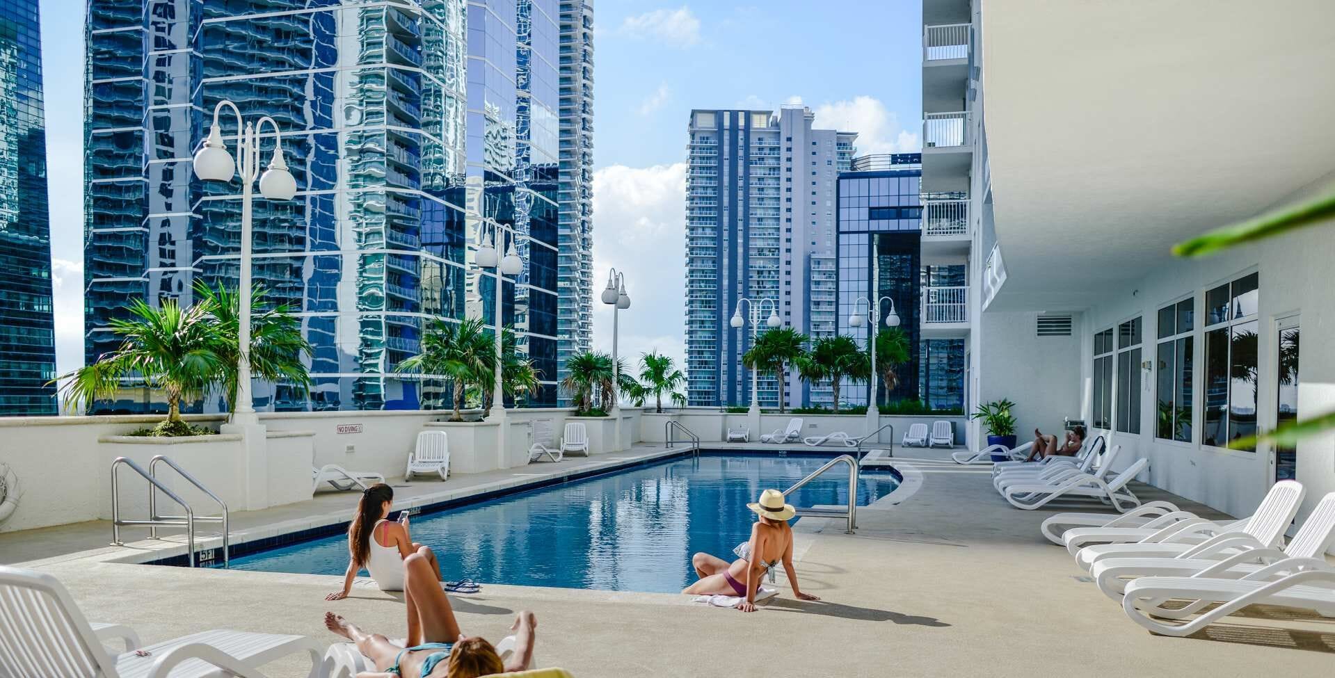 A rooftop pool area with lounge chairs, a swimming pool, and high-rise buildings in the background.