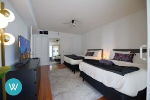 A modern hotel room with two beds, a flat-screen TV, a ceiling fan, and a view of the cityscape through the window. - Stylish 1BR | Free Parking | Near Kaseya Center (Miami)