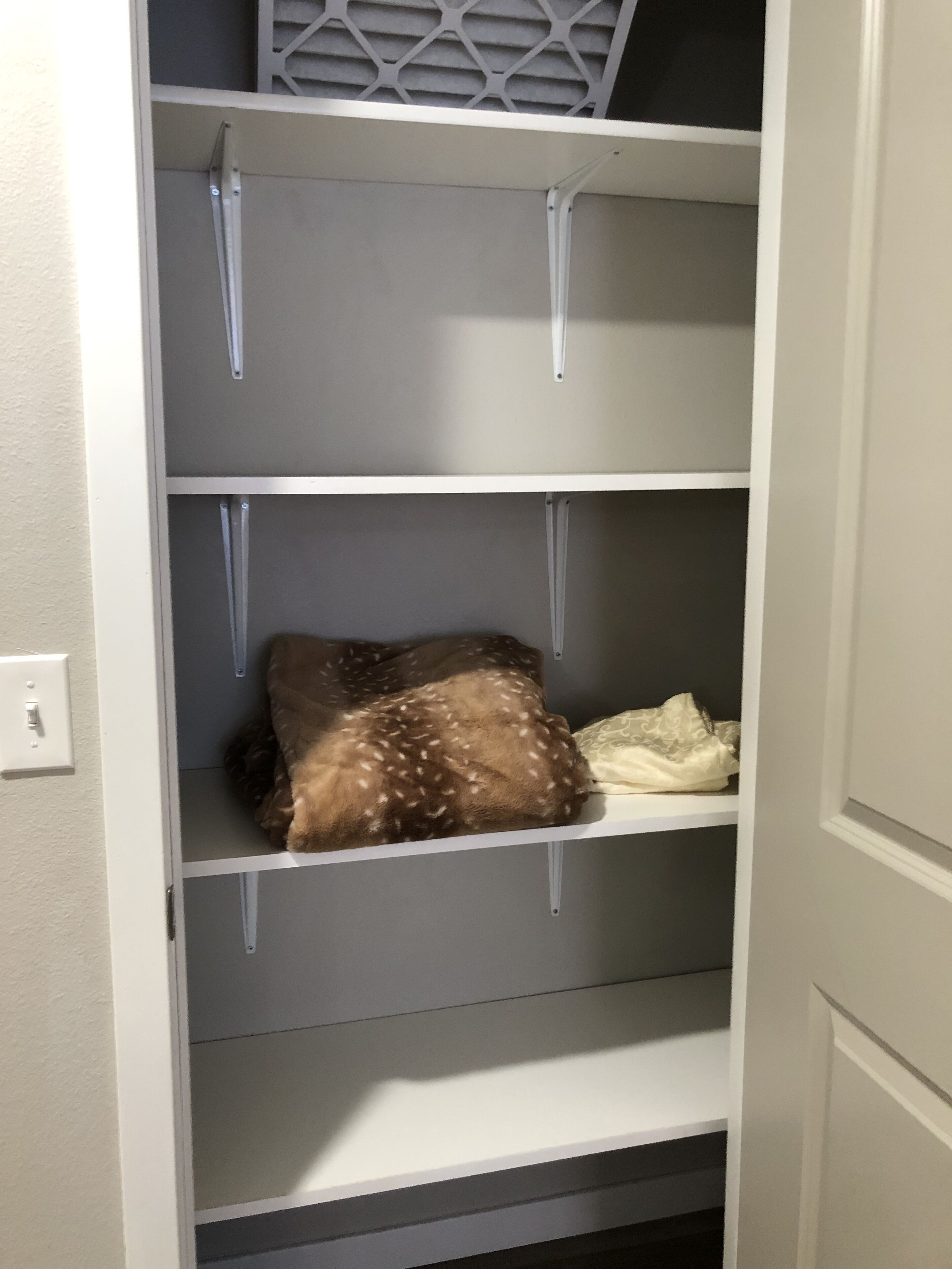 A closet with three shelves, a hanging rod, and a light switch.