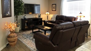 A living room with a brown leather sofa, a flat-screen TV, a fireplace, a large plant, and a rug.