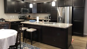 A modern kitchen with dark cabinets, stainless steel appliances, a marble countertop, and a central island with stools.