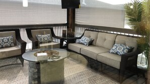 An outdoor seating area with wicker furniture, a stone table, and a television mounted on the wall.