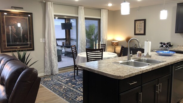 A modern kitchen with a large island, dark cabinetry, and a dining area with a view to the outdoors.