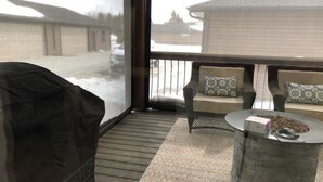 A covered outdoor seating area with a stone table, two cushioned chairs, and a fire pit.