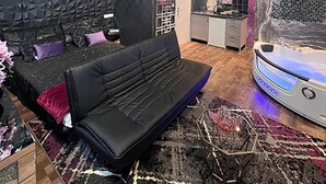 A modern room with a black textured wall, a black sofa, a patterned rug, a chandelier, and a spa tub. - Urban Suite With Jaccuzzi on Shopping Street (Wien)