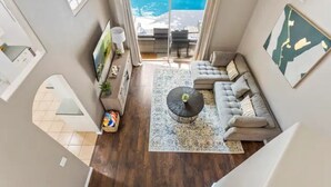 Una sala de estar moderna con un gran ventanal que da a un balcón, un sofá gris, una alfombra estampada y una mesita de centro.