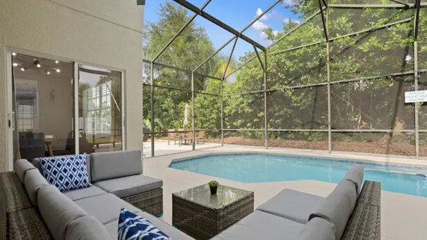 Zona de piscina con terraza techada, mobiliario exterior y vistas a los árboles circundantes.
