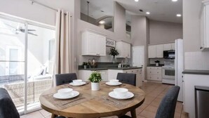 Una cocina moderna con armarios blancos, una mesa de comedor para cuatro personas y un balcón con vistas.