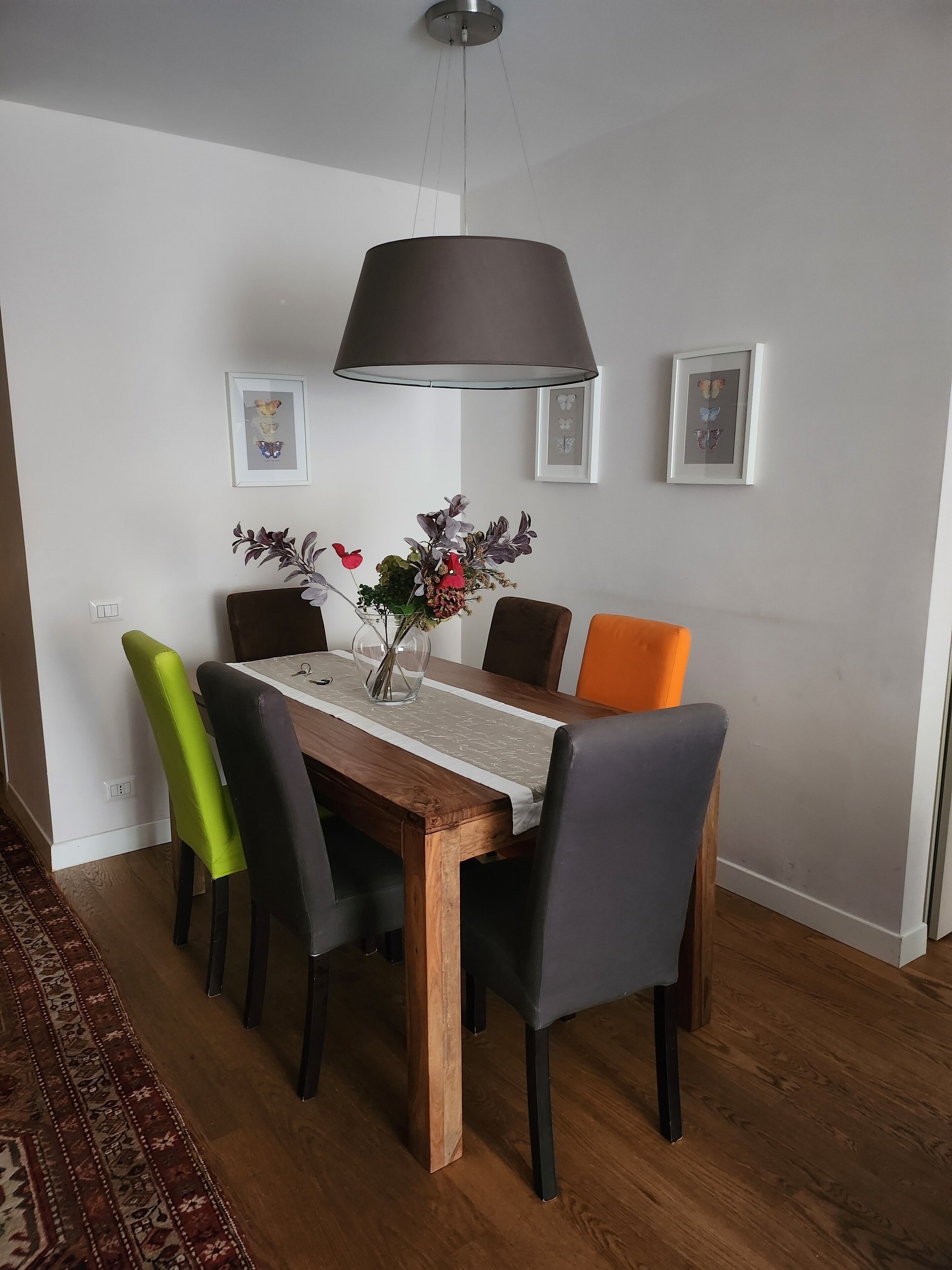 A dining area with a wooden table, six chairs, a hanging light fixture, and two framed pictures on the wall.