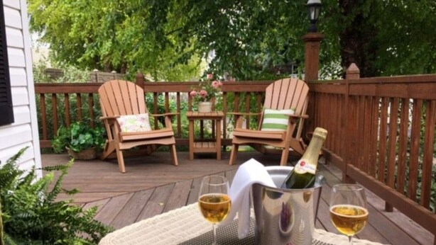 Une terrasse en bois avec des meubles en osier, une bouteille de champagne et des verres de vin.