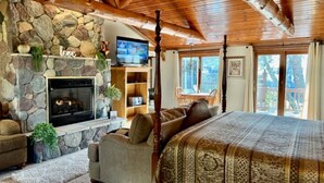 Une pièce chaleureuse avec une cheminée en pierre, un grand lit recouvert d’une couvre-lit à motifs, une télévision et un mur en pierre.