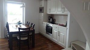 A kitchen with white cabinets, a dining table with chairs, a microwave, and an oven. - Cozy vacation home for up to 5 people in a quiet location in Greetsiel (Krummhörn)