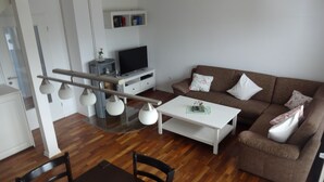 A modern living room with a brown sofa, white coffee table, and a TV on a stand. - Cozy vacation home for up to 5 people in a quiet location in Greetsiel (Krummhörn)