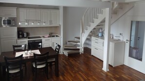 A modern kitchen with white cabinetry, a dining table with chairs, and a wooden staircase. - Cozy vacation home for up to 5 people in a quiet location in Greetsiel (Krummhörn)