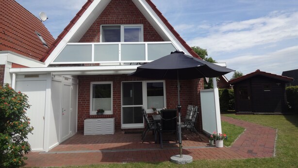 A two-story house with a red brick facade, white trim, and a triangular roof. - Cozy vacation home for up to 5 people in a quiet location in Greetsiel (Krummhörn)