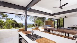 Una cocina moderna con una isla grande, un comedor con una mesa larga y vistas al océano.