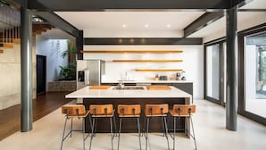 Una cocina moderna con una isla central, taburetes de bar y una pared decorativa de piedra.