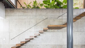 Una escalera de hormigón con escalones de madera y barandillas de metal, que sube a un piso superior.