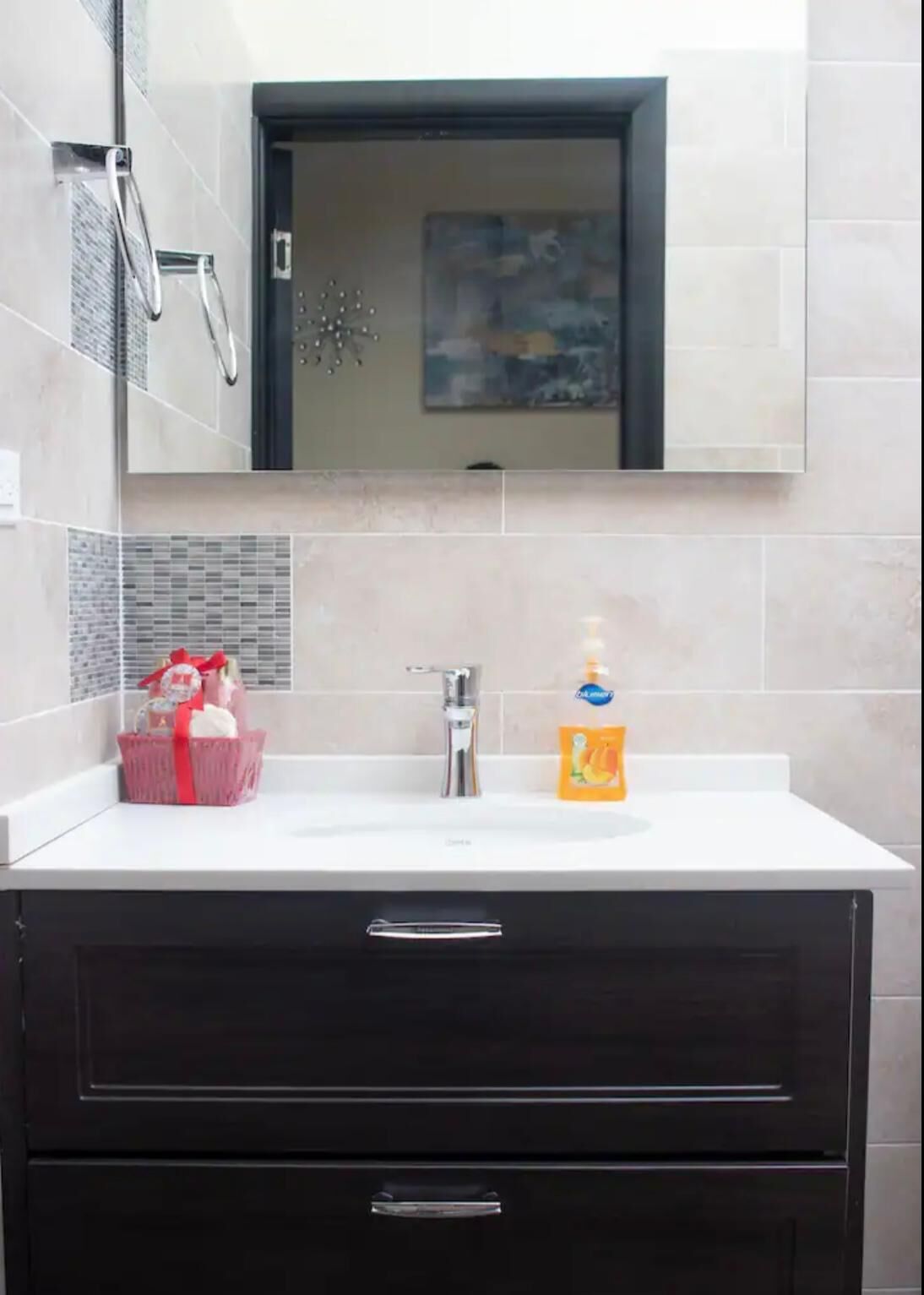Een moderne badkamer met een witte wastafel, een donker kastje eronder, en een douche met een glazen deur.