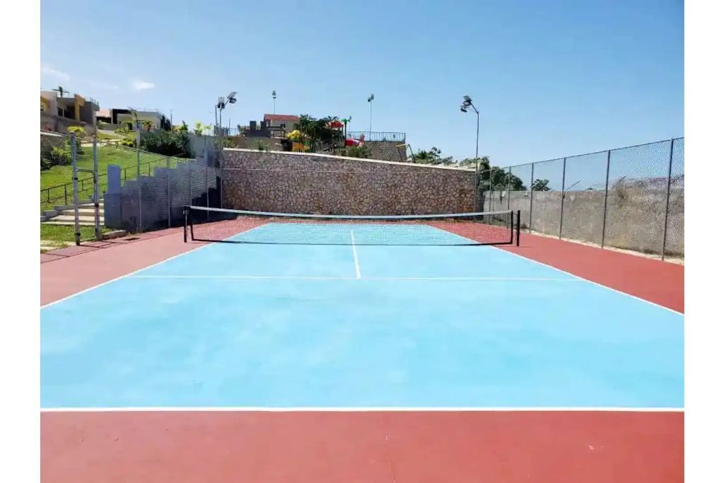 Un court de tennis en plein air, doté d’un filet, entouré d’un mur de pierre et d’une clôture.