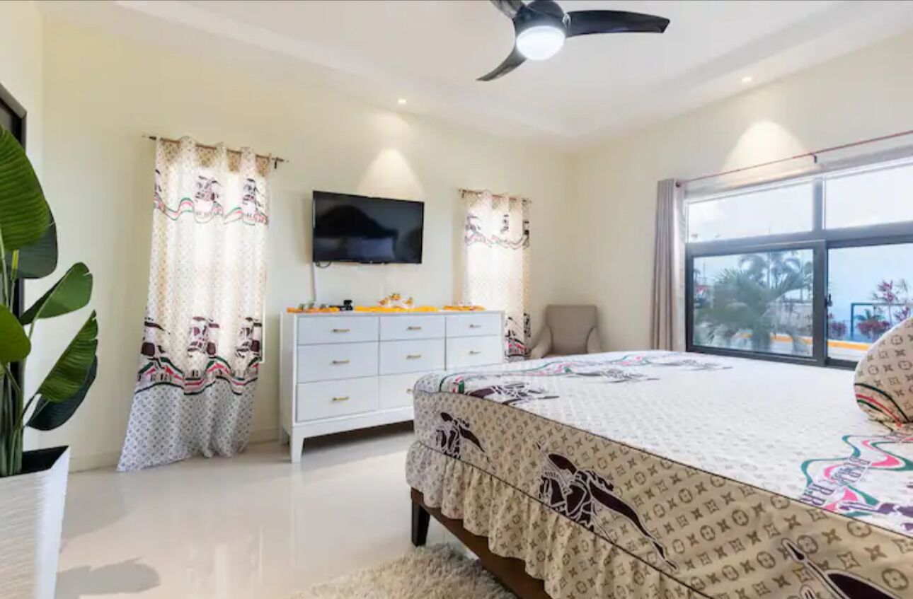 Ein Schlafzimmer mit Bett, Fernseher, Kommode und einem Fenster mit Blick.
