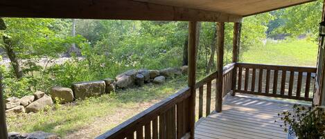 A wooden deck with a railing, overlooking a natural landscape with rocks and greenery.