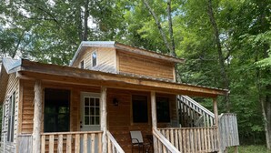 A wooden cabin with a porch, a staircase, and a potted plant.