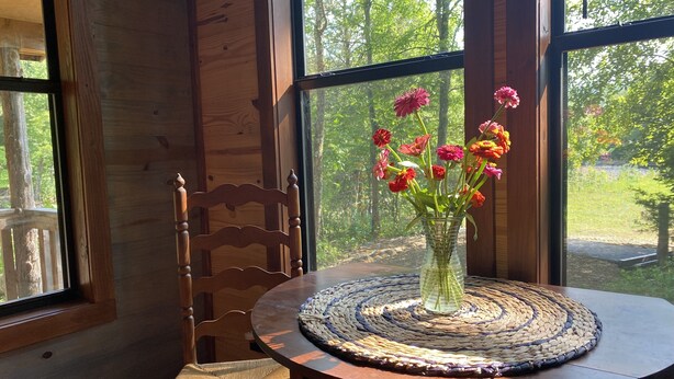 A wooden interior with a round table, a woven placemat, and a vase with flowers.