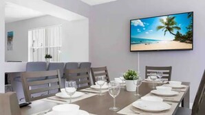 Un coin repas avec une longue table dressée pour six personnes, des assiettes blanches et des verres à vin.