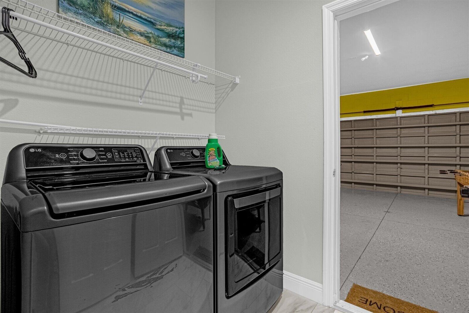 A laundry area with two stacked washers and dryers, a green bottle of detergent, and a painting on the wall.
