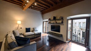 A modern living room with a wooden ceiling, a sofa set, a flat-screen TV mounted on the wall, and a balcony with a view of buildings. - Piazza Navona Mara’s apartment (Roma)