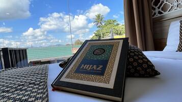 A neatly made bed with a framed book titled "HIJAZ" and a patterned pillow.