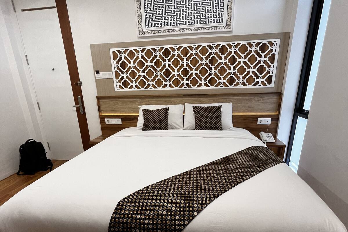 Quarto de hotel com uma cama grande, cabeceira de madeira, painel decorativo na parede e uma janela.