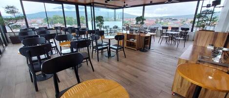 A spacious indoor area with multiple seating arrangements, including tables and chairs, and a view of a cityscape through large windows.