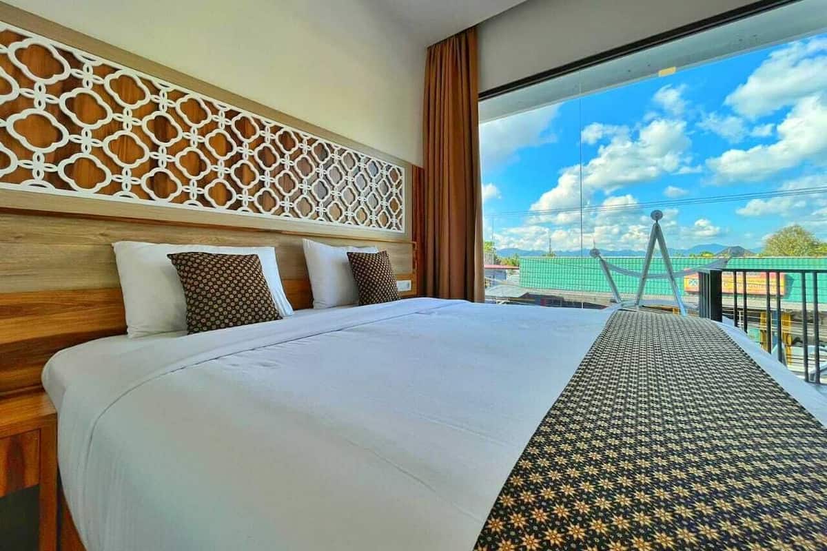 Quarto de hotel com uma cama grande, cabeceira decorativa e vista para o céu e prédios.